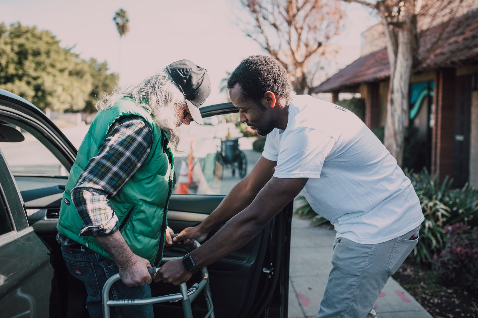 A caregiver helping someone with a walker get into a car outdoors